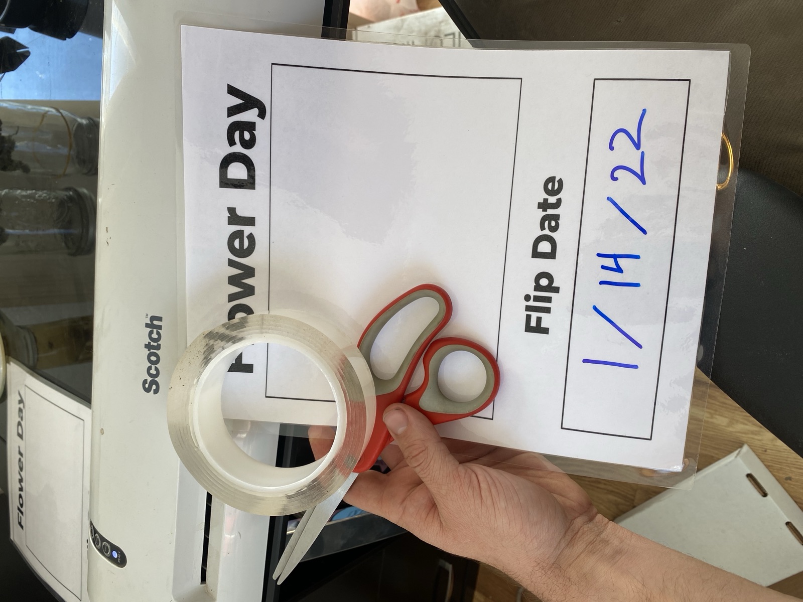 Laminated door card from Wildcreek Farms — printed fields for Flower Day and Flip Date, with '1/14/22' handwritten in blue marker. Scissors and tape in hand, mid-assembly.
